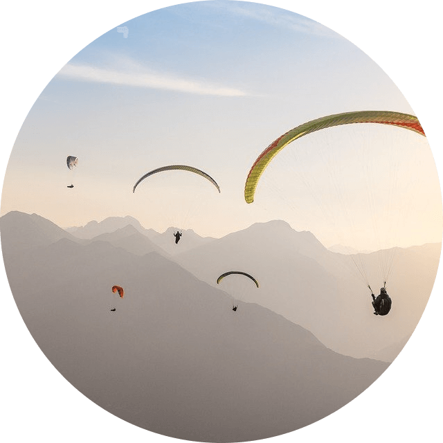 Mehrere Paragleiter in Sonnenaufgangsstimmung mit Bergen im Hintergrund