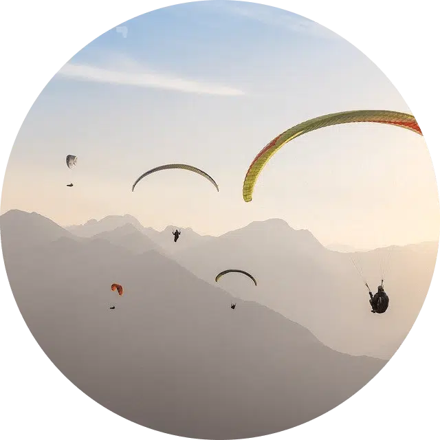 Mehrere Paragleiter in Sonnenaufgangsstimmung mit Bergen im Hintergrund